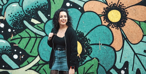 student standing in front of a large wall mural and smiling. 